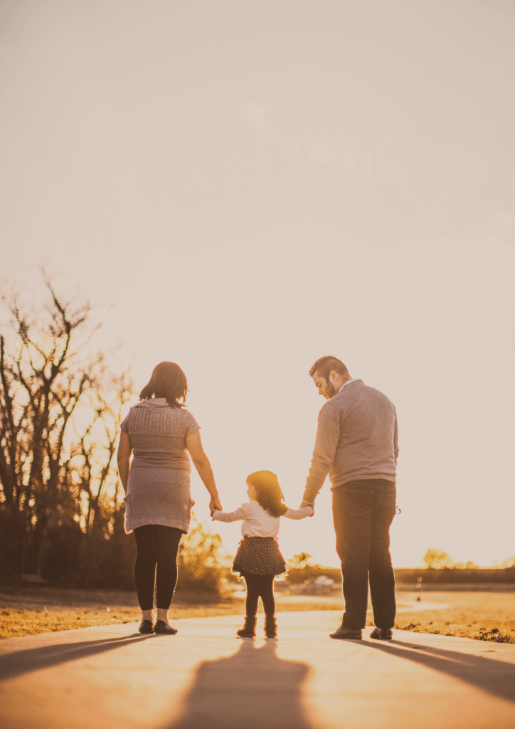 Photo d'une famille de dos sur un chemin au couché du soleil avec une maman, une enfant et un papa